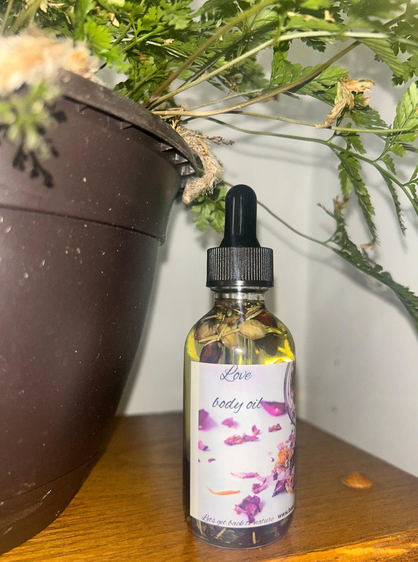Love Body Oil Natural Moisturizing Glow Oil bottle next to a potted plant, showcasing its herbal ingredients.